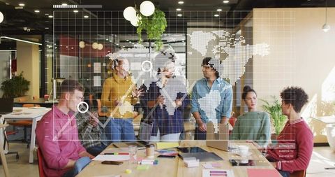 Team Collaborating Around Laptops with World Map Data Overlay in Modern Open-Plan Office