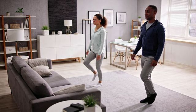 Couple exercising at home in modern minimalist living room wearing hoodies on gray rug