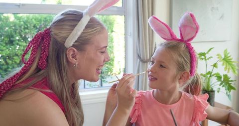 Mother painting daughter's nose while wearing bunny ears for playful easter family bonding at home