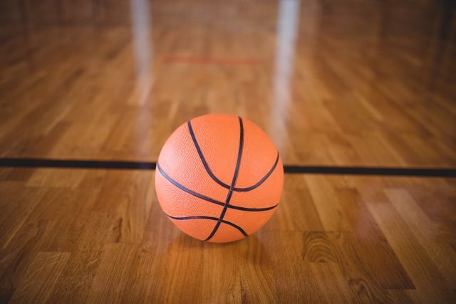 This image shows a close-up of a basketball on a wooden court, perfect for use in sports-related content, athletic promotions, basketball training materials, or recreational activity advertisements.
