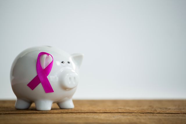 Close-up of pink Breast Cancer Awareness ribbon on piggybank over wooden table against white background