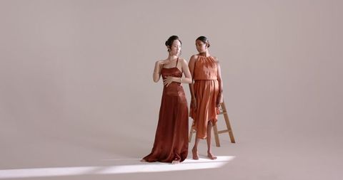 Elegant asian models in satin gowns against beige backdrop
