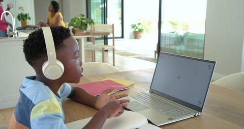 African american child learning with headphones at sunlit open-plan kitchen table