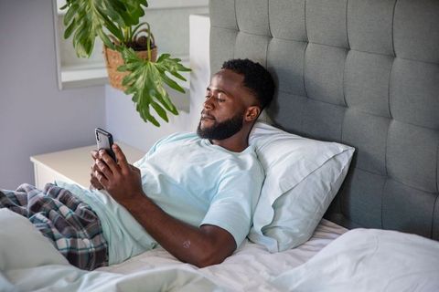 Man Relaxing on Bed Using Smartphone at Home