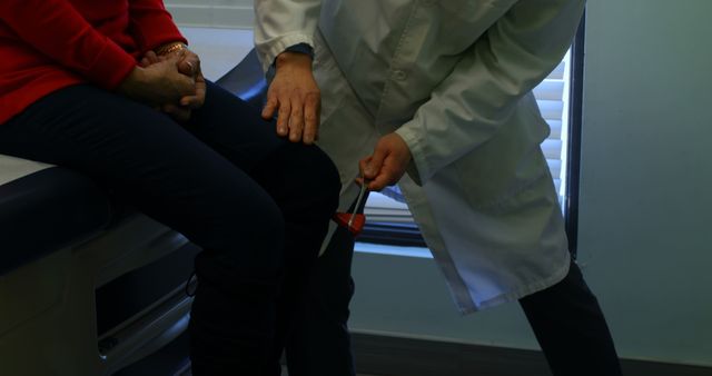 Doctor performing knee reflex test on patient in medical examination room. Useful for healthcare articles, medical care promotions, clinic advertisements, or informational content about medical check-ups.