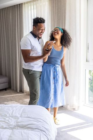 Couple laughing while reading smartphone message in sunlit bedroom