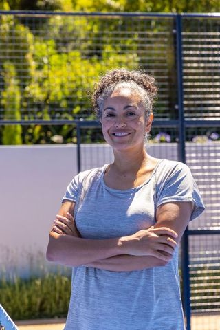 Confident african american woman standing arms crossed smiling on outdoor sports court