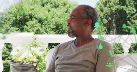 Relaxed Man Sitting on Patio with Digital Symbols Overlaying nature