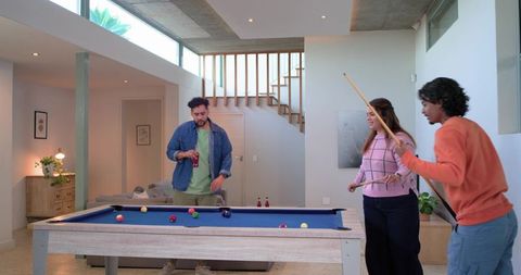 Friends playing pool in modern loft living space with blue-felt billiards table and drinks