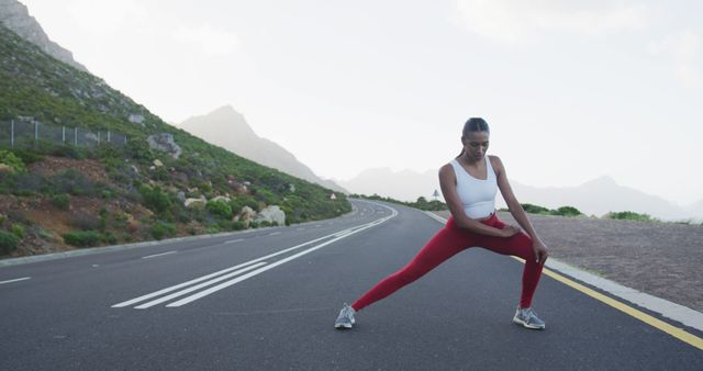 Woman stretching on open road in mountains with white sports top and red leggings - Download Free Stock Images Pikwizard.com