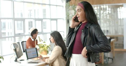 Indian Businesswoman Talking on Phone in Bright Open-Plan Office with Collaborative Team