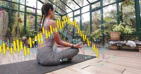 Young Woman Meditating in Glasshouse Wearing Smartwatch Displaying Financial Charts Overlay