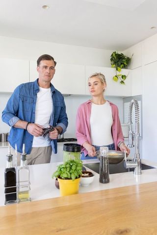 Couple standing washing basil at modern kitchen island during bright casual meal prep