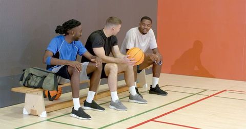 Basketball teammates resting and chatting on courtside bench holding ball and water bottle