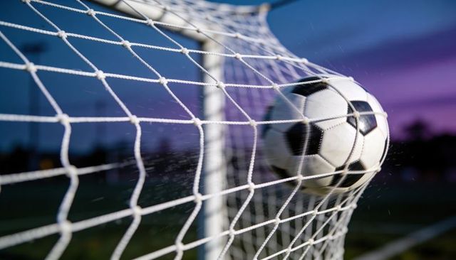 Soccer ball hitting goal net at dusk showing motion, net impact and stadium atmosphere