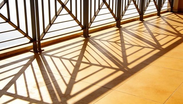 Sunlit Metal Railing Casting Geometric Shadow Pattern Across Warm Terracotta Terrace Tiles