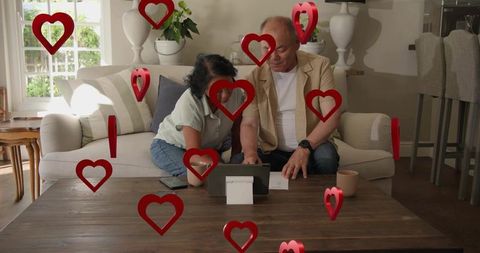 Mature couple using tablet together at home amid floating red hearts sharing connection