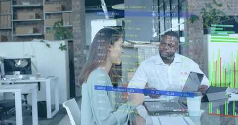 Business team analyzing market charts on glass partition using laptops and tablet