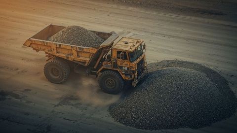 Cat dumper truck unloading gravel in quarry site at dusk