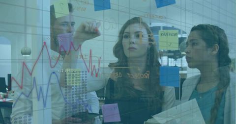 Team collaborating and drawing analytics on glass board with sticky notes in modern office