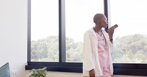 African american clinician speaking into smartphone for telemedicine by clinic window