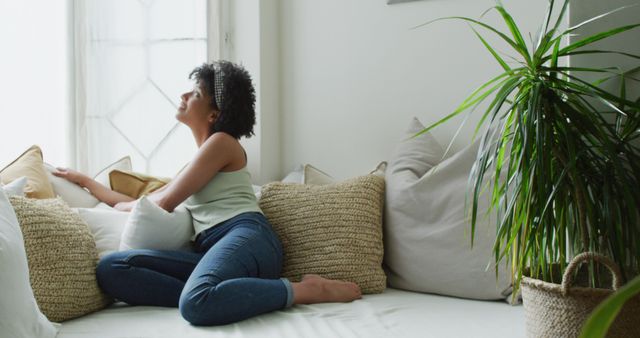 Image of happy biracial woman relaxing at home, sitting on sofa, with copy space. Happiness, relaxation and domestic life.