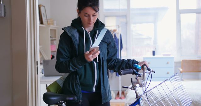 Young Woman Checking Smartphone While Holding Bicycle Indoors - Download Free Stock Images Pikwizard.com