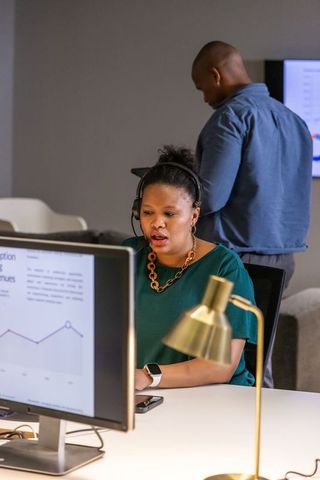 African american woman wearing headset reviewing analytics on monitor in modern office