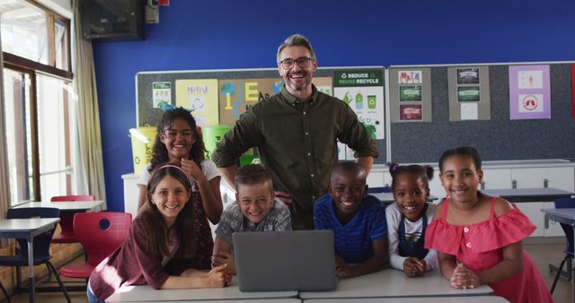 Portrait of happy diverse male teacher and group of schoolchildren looking at laptop. children at primary school in summer.