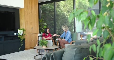 Two women recording cozy living room podcast - asian senior guest and host interviewing