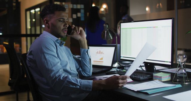 Image of biracial businessman talking on smartphone and using computer at night in office - Download Free Stock Photos Pikwizard.com