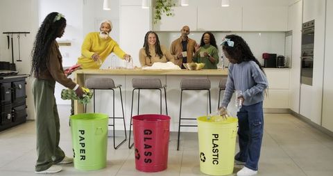Multigenerational Black family sorting paper glass plastic recyclables in bright modern kitchen