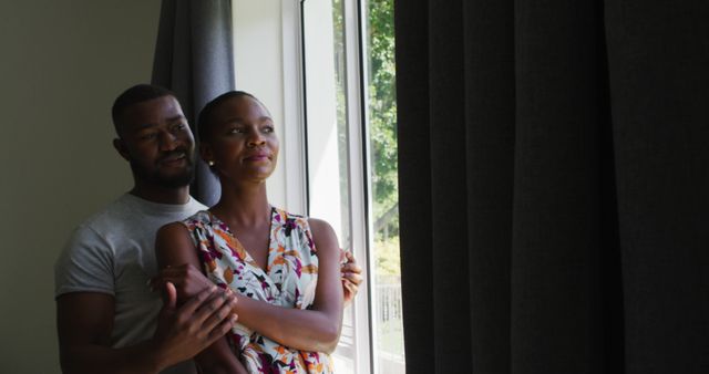 African american couple embracing each other while looking out of the window at home. couple relationship lifestyle concept