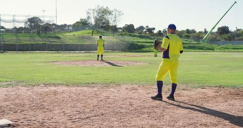 Baseball Team Preparing on Sunlit Field in Bright Yellow Uniforms with Pitcher on Mound