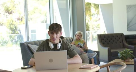 Teen studying and typing on laptop in modern minimalist living room with headphones
