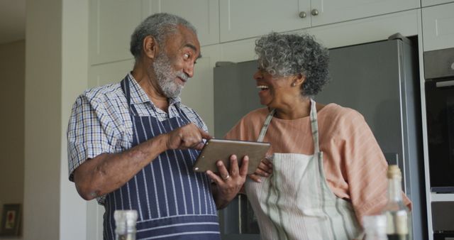 Happy african american senior couple cooking together, using tablet. healthy, active retirement lifestyle at home.