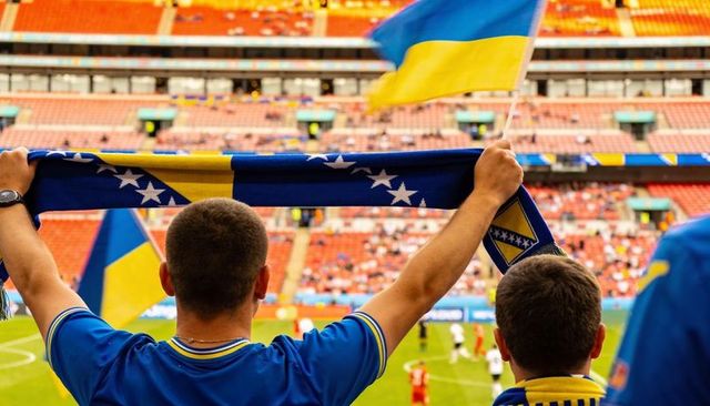 Fans holding bosnia scarves and waving ukraine flags cheering in soccer stadium