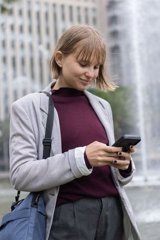 Young professional texting on smartphone by urban fountain during overcast commute