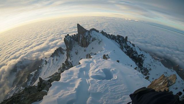 Climbing alpine summit ridge at sunrise above cloud inversion with jagged peaks