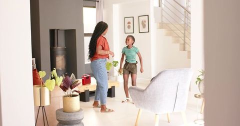 African mother and teenage daughter talking in bright modern living room with plants