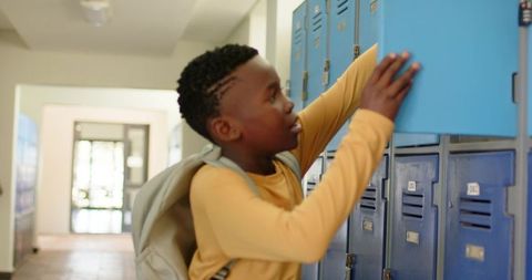 African teen boy opening blue locker in school hallway wearing backpack