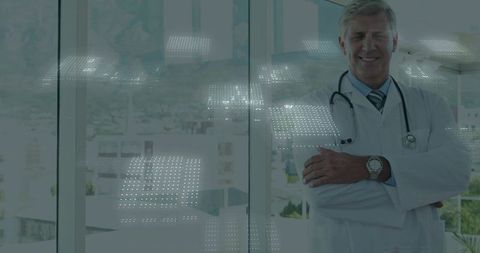 Confident male doctor standing arms crossed wearing stethoscope in modern clinic with city view