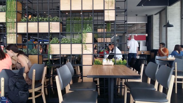 Casual dining environment featuring modern and urban design elements, including green plants and open lattice partitions. Ideal for use in content related to restaurant design, urban lifestyle, social environments, and contemporary dining spaces.