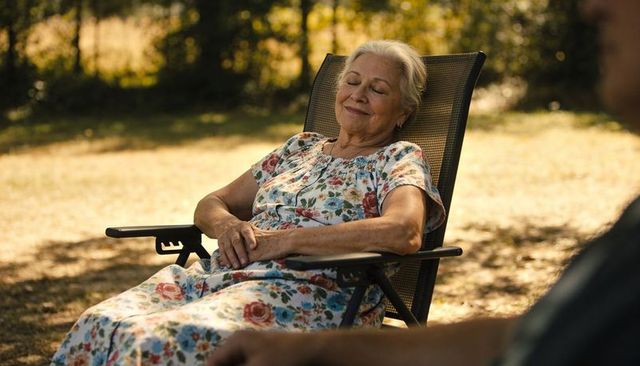 Senior woman relaxing in floral dress on mesh lawn chair under warm dappled sunlight