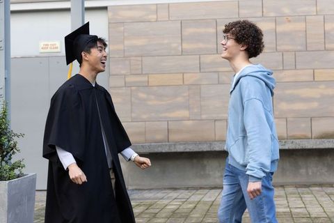 Diverse friends celebrating college graduation in gown and cap laughing on campus plaza