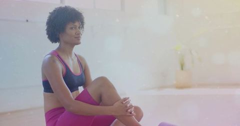 Woman sitting on yoga mat holding knee during gentle stretch in bright studio low-impact workout