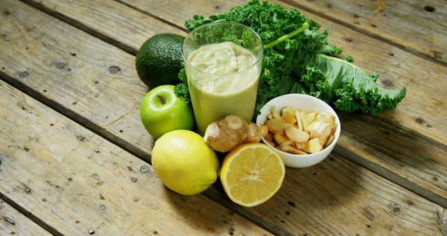 A variety of fresh ingredients including avocado, kale, apple, lemon, and ginger are arranged on a wooden surface, showcasing components for a healthy green smoothie. Vibrant colors and textures emphasize the freshness and nutritional value of the produce.