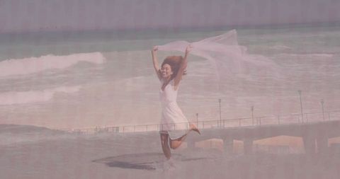 Joyful woman leaping by ocean with translucent scarf