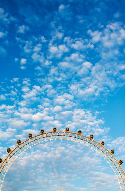 Ferris wheel extending into vibrant blue sky filled with white, fluffy clouds. Ideal for travel, tourism, and leisure-related content or emphasizing fun, outdoor activities.