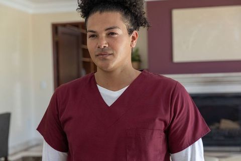 Mid-adult man standing in living room wearing maroon medical scrubs and white undershirt
